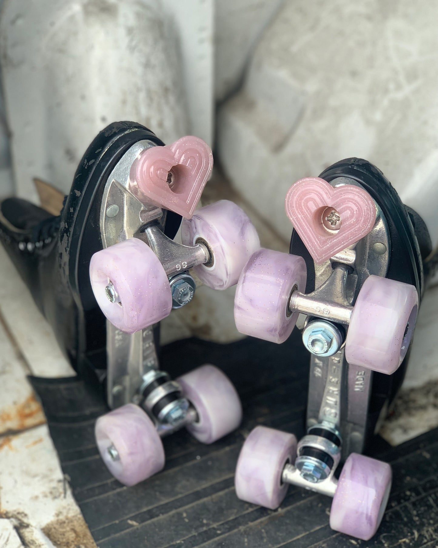 pair of black roller skates with light pink wheels and bbpink bolt-on heart shaped toe stops on a light gray and black background