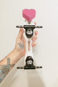 pink color heart shaped roller skate toe stop on a roller skate plate with roller skate trucks pictured carried in hand on a white background