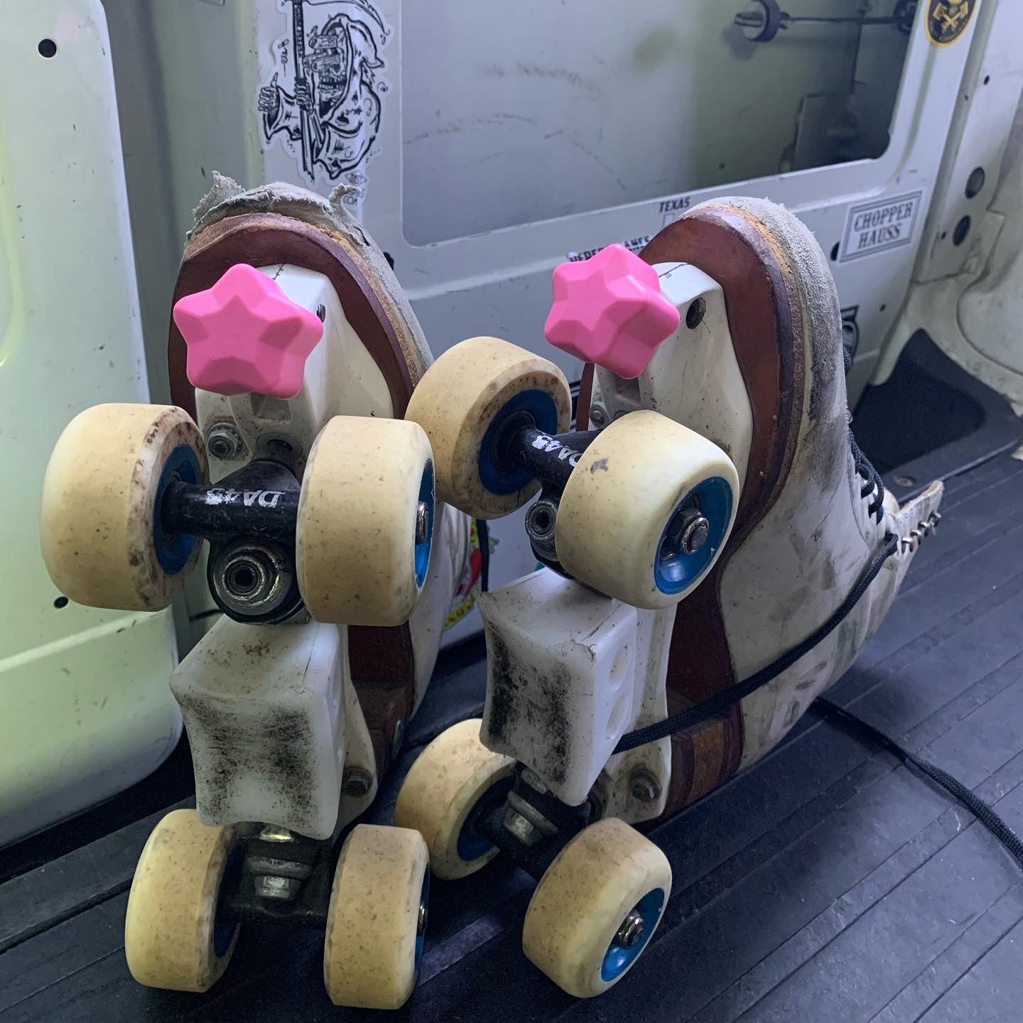 pink color roller skate toe stop in the shape of a five point star on a pair of white roller skates. the wheels on the roller skates are light tan with a blue center. the set of skates is placed in front of a black and white background.