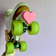 Load image into Gallery viewer, pink color heart shaped roller skate toe stop on a roller skates with green wheels pictured carried in hand on a white background